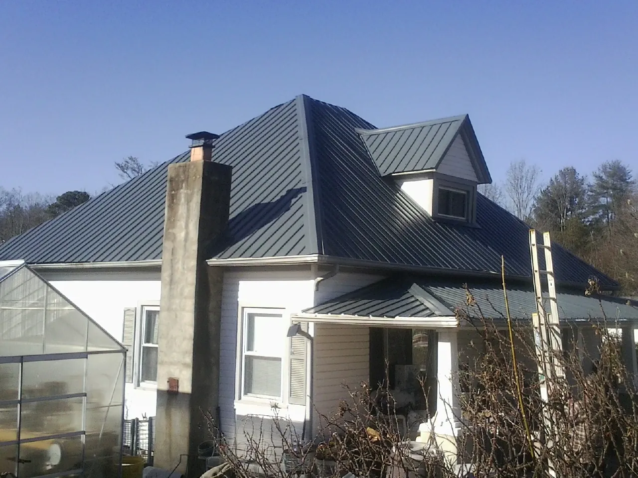 Dark blue standing seam metal roof on a white farmhouse with dormer — Slate & Tile Roof Repair by Roofing Brothers in Lorimor