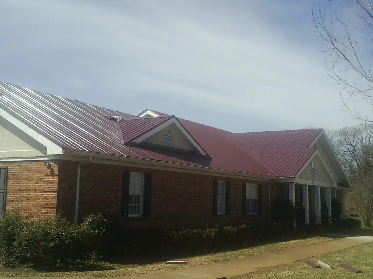 Red metal roof with gabled entries on a long brick building, from a Hail Damage Roof Repair job in Lorimor