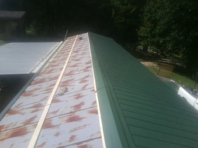 Old rusted panels beside newly installed green metal roofing — Wind Damage Roof Repair by Roofing Brothers in Lorimor