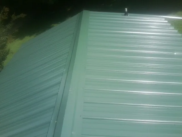 New green metal panels meeting at the ridge of a roof — Flat Roof Repair work by our crew in Lorimor