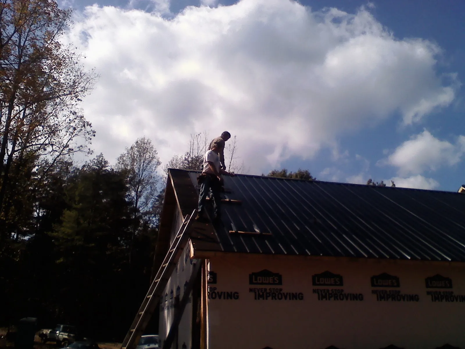 Roofer fastening dark metal panels high against a cloudy sky, from a Roof Inspection job in Lorimor
