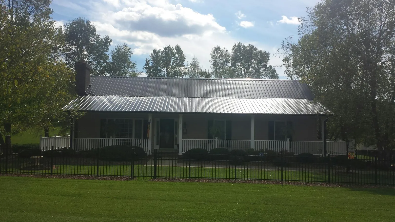 Gray metal roof on a brick ranch with a full width front porch — Gutter Guard Installation work by our crew in Lorimor